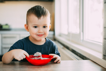 A child in the kitchen eating their own oatmeal with a red plate