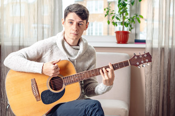 Young attractive musician sitting on a chair playing acoustic guitar. Concept of music as a hobby