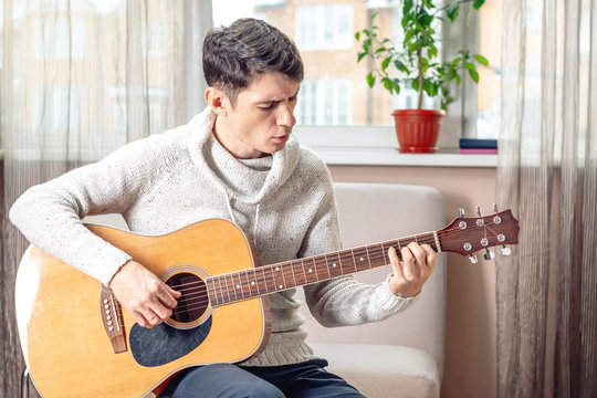 Young attractive musician sitting on a chair playing acoustic guitar. Concept of music as a hobby