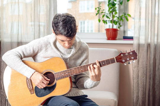 Young attractive musician sitting on a chair playing acoustic guitar. Concept of music as a hobby