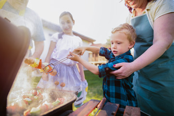 Cute little boy train to turn meat on barbeque grill.Other members of family standing around him...