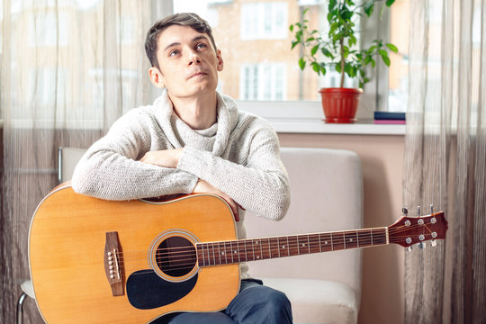 Young attractive male musician sitting on a chair holding an acoustic guitar. Concept of music as a hobby