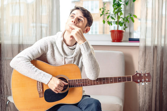 Young attractive male musician sitting on a chair holding an acoustic guitar. Concept of music as a hobby