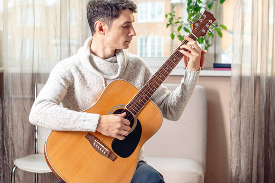 Young attractive male musician sitting on a chair playing acoustic guitar. Concept of music as a hobby