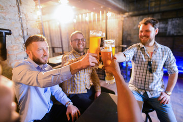 Group of young happy man sitting in a pub and clinking with glasses full of bear. Man night out.