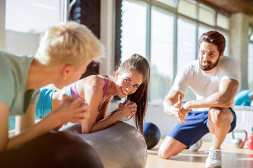 Two fit sporty girls doing exercises with pilates balls in gym while personal fitness trainer is...