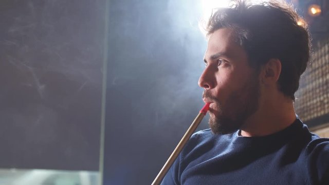 Bearded attractive cheerful man in fashion outfit thinking about something while smoking.