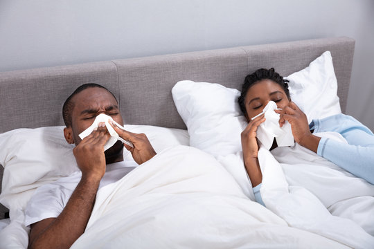 Sick Couple Lying On Bed Blowing Their Nose