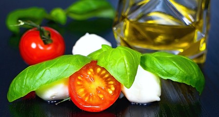 Ingredients for the preparation of Caprese Mediterranean salad: tomatos, mozzarella, basil leaves and olive oil.