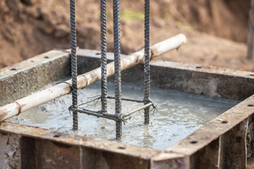 Pouring concrete into steel box for foundation pillar in process of house building