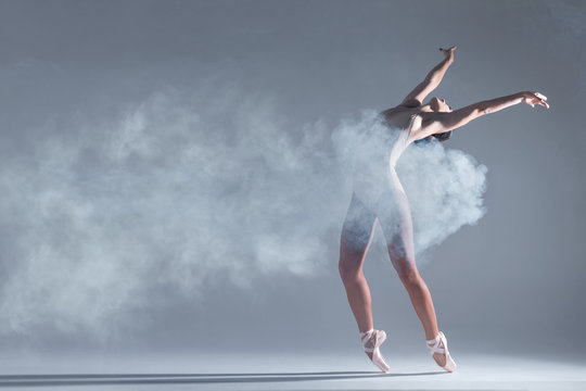 Elegant Woman Female Girl Ballerina Dancer In Beige Body Pointe Shoes Dancing, Making Performance And Dance Element In Fog Dust Smoke Fume On Isolated Grey Background Scene. Dancing In Cloud Concept