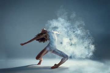 Dancing in cloud concept. Muscle brunette beauty female girl adult woman dancer athlete in fog smoke fume wearing dance bodysuit making emotional dance element performance on isolated grey background
