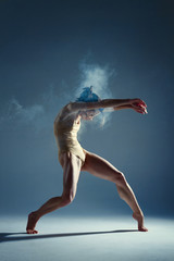 Dancing in cloud concept. Muscle brunette beauty female girl adult woman dancer athlete in dust / fog. Girl wearing dance bodysuit making dance element performance on isolated grey / black background
