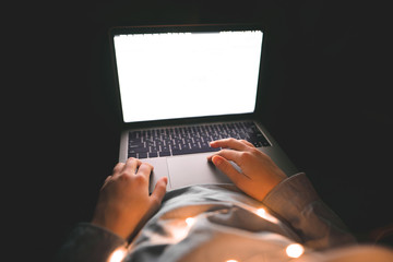 Photo of female hands on a touch screen of a laptop with a white screen. Woman working on a laptop at night in bed, focus on hands. Work for a laptop.