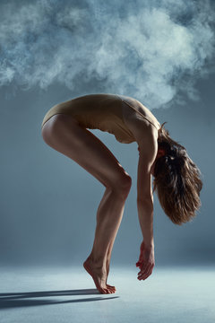Dancing in cloud concept. Muscle brunette beauty female girl adult woman dancer athlete in dust / fog. Girl wearing dance clothing making dance element performance on isolated grey / black background
