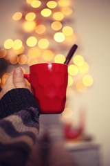 woman's hand with mug of hot drinc against  blurred christmas tree background/christmas  concept