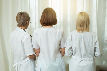 three women doctor in white coats stand back in the clinic