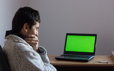 Young man home sick by chroma key laptop. Person with hand on throat looking at green screen computer on desk. Tele health concept