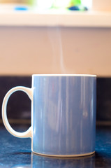 A mug on a kitchen worktop with steam coming out of the top.