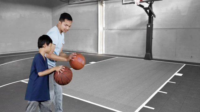 JAKARTA, Indonesia - January 08, 2019: Little boy and his father learn how to shoot with a basketball at indoors basketball court. Shot in 4k resolution