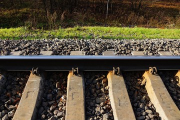 Obraz premium part of the railroad with an iron rail and concrete sleepers in small gray rubble and green grass on the side of the road