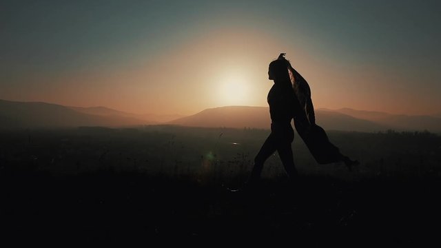 Silhouette of a beautiful young woman running in the mountains with a pareo in her hands. Slow motion. The concept of freedom, ease, success, rest. Sunset