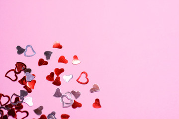 Silver and red shiny design hearts on pink neutral background with empty space for image or text. Confetti for romantic happy valentines day. holiday hearts made of silver paper. 