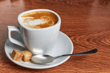 coffee with a pattern of foam is in the saucer, which is a teaspoon and two pieces of cane sugar
