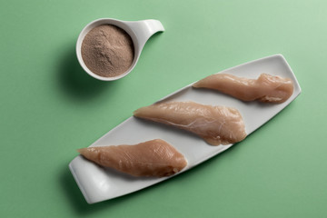 Raw chicken breasts and a whey protein scoop chocolate flavor. Sport nutrition. Green background. Top view