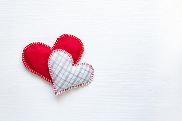 Two fabric hearts on white wooden background, from above
