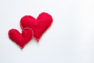 Two red fabric hearts on white wooden background, from above