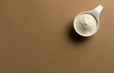 Whey protein powder sports bodybuilding supplement. Top view white porcelain scoop with vanilla flavor powder. Brown background and copy space