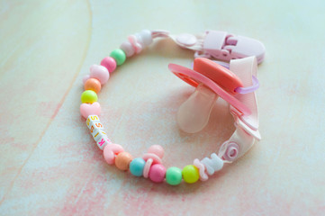 Baby pacifier with holder on a pink background