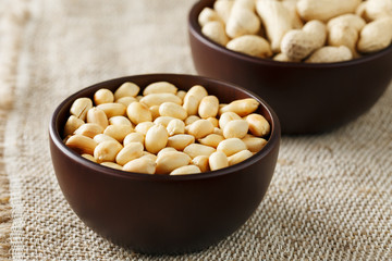 Peanuts in the shell and peeled close-up in cups. Roasted peanuts in their shells and peeled against a brown cloth.