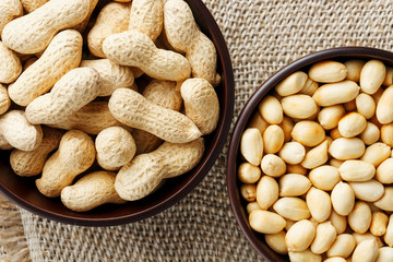 Peanuts in the shell and peeled close-up in cups. Roasted peanuts in their shells and peeled against a brown cloth.