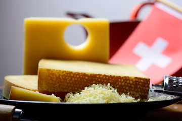 Assortment of Swiss cheeses Emmental or Emmentaler medium-hard cheese with round holes, Gruyere, appenzeller and raclette used for traditional cheese fondue and gratin and flag of Switzerland
