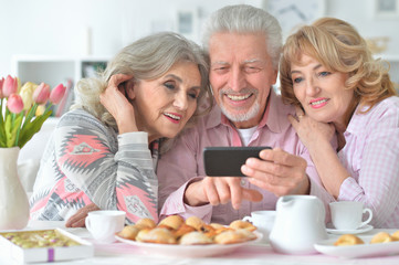 Portrait of happy senior people with smartphone drinking tea