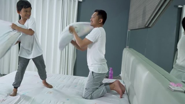 Happy little boy having pillow fight with his father on the bed in the morning at home. Shot in 4k resolution