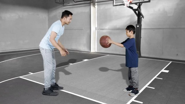 JAKARTA, Indonesia - January 08, 2019: Young man teaching his son to play basketball at indoors basketball court. Shot in 4k resolution