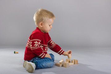 Little boy playing with wooden cubes sitting on the floor.