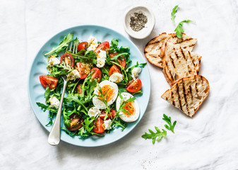 Breakfast salad - arugula, cherry tomatoes, mozzarella and boiled egg with olive oil, mustard, lemon dressing on a light background, top view