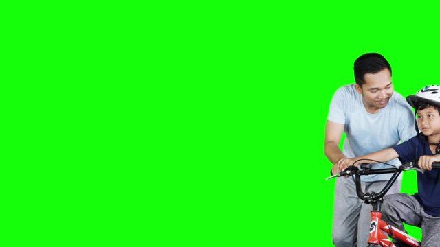Cute little boy learns to ride bicycle with his father. Shot in 4k resolution with green screen background in the studio
