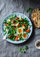Breakfast salad - rocket, cherry tomatoes, mozzarella and boiled egg with olive oil, mustard, lemon dressing on a grey background, top view