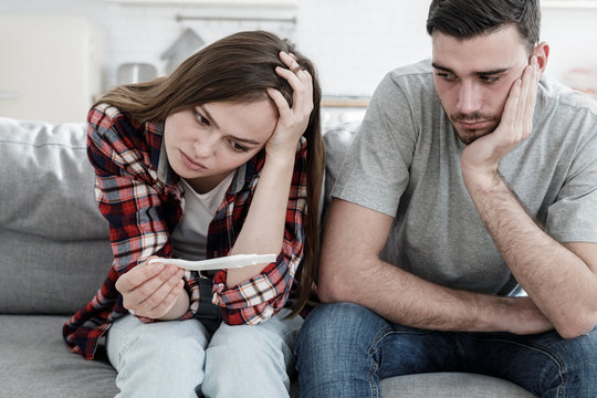 Young couple worried because of positive result of pregnancy test, looking upset