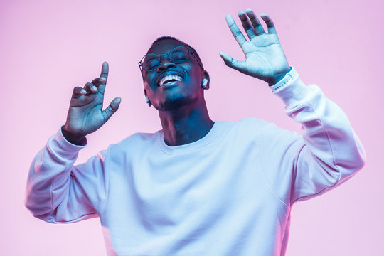Young african man listening to music with wireless earphones and dancing isolated on pink background