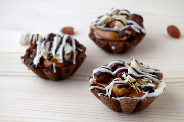 Tartlets  are made of a biscuit and filler from caramel, chocolate and nuts. Cakes are on a wooden surface.