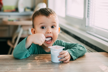 child eating yogurt in the kitchen in a green jacket, daylight