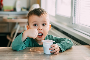 child eating yogurt in the kitchen in a green jacket, daylight