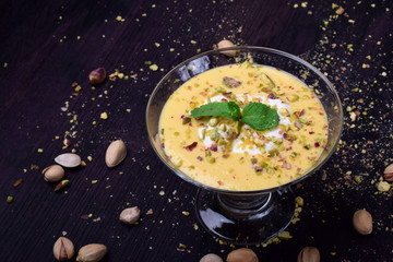 Mango yogurt dessert in an ice-cream bowl topped with pistachios and mint against the dark background - obrazy, fototapety, plakaty