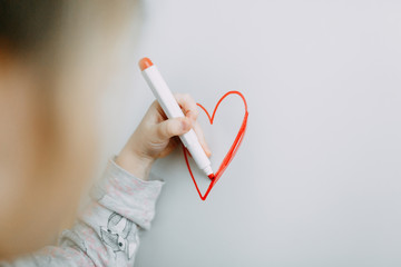 Girl draws heart with marker on a white blackboard. Mothers Day. Valentine's Day